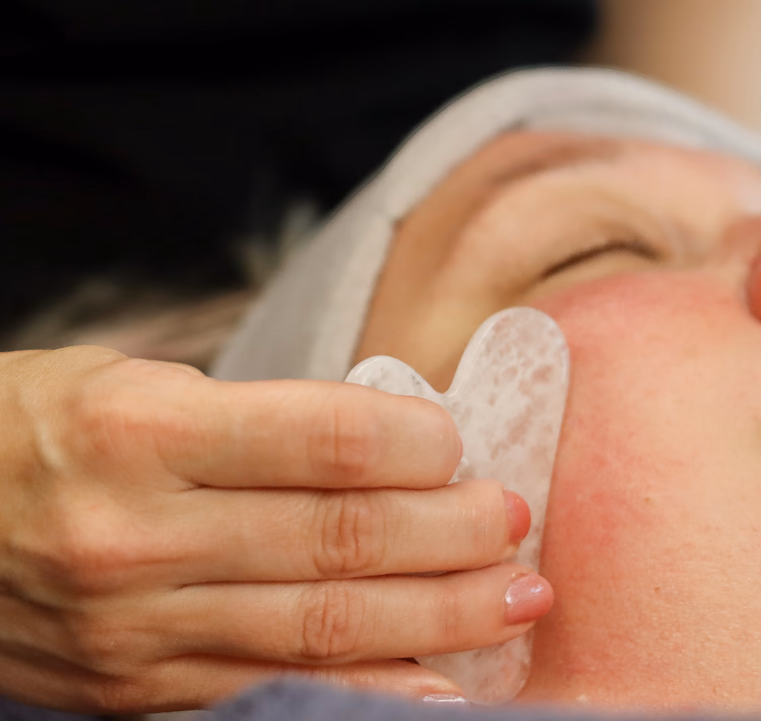 Kosmetologi hieroo asiakkaan poskea Gua Sha -kivellä kasvohoidon aikana